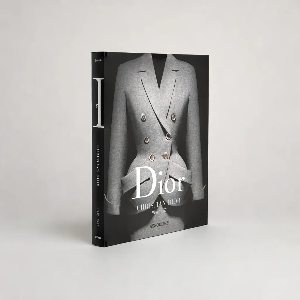 Boken "Dior by Christian Dior" av New Mags har en grå skräddarsydd jacka med flera knappar, som symboliserar haute couture. Den pryder elegant både främre och bakre omslag, med märkets namn markerat mot en ljusgrå bakgrund.